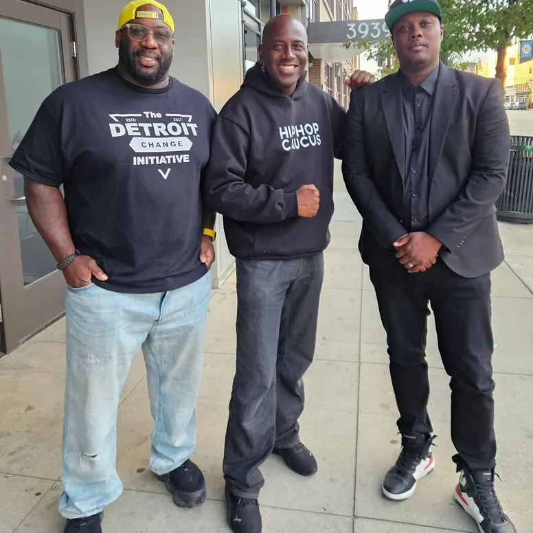 Three men standing on a sidewalk in front of a building.